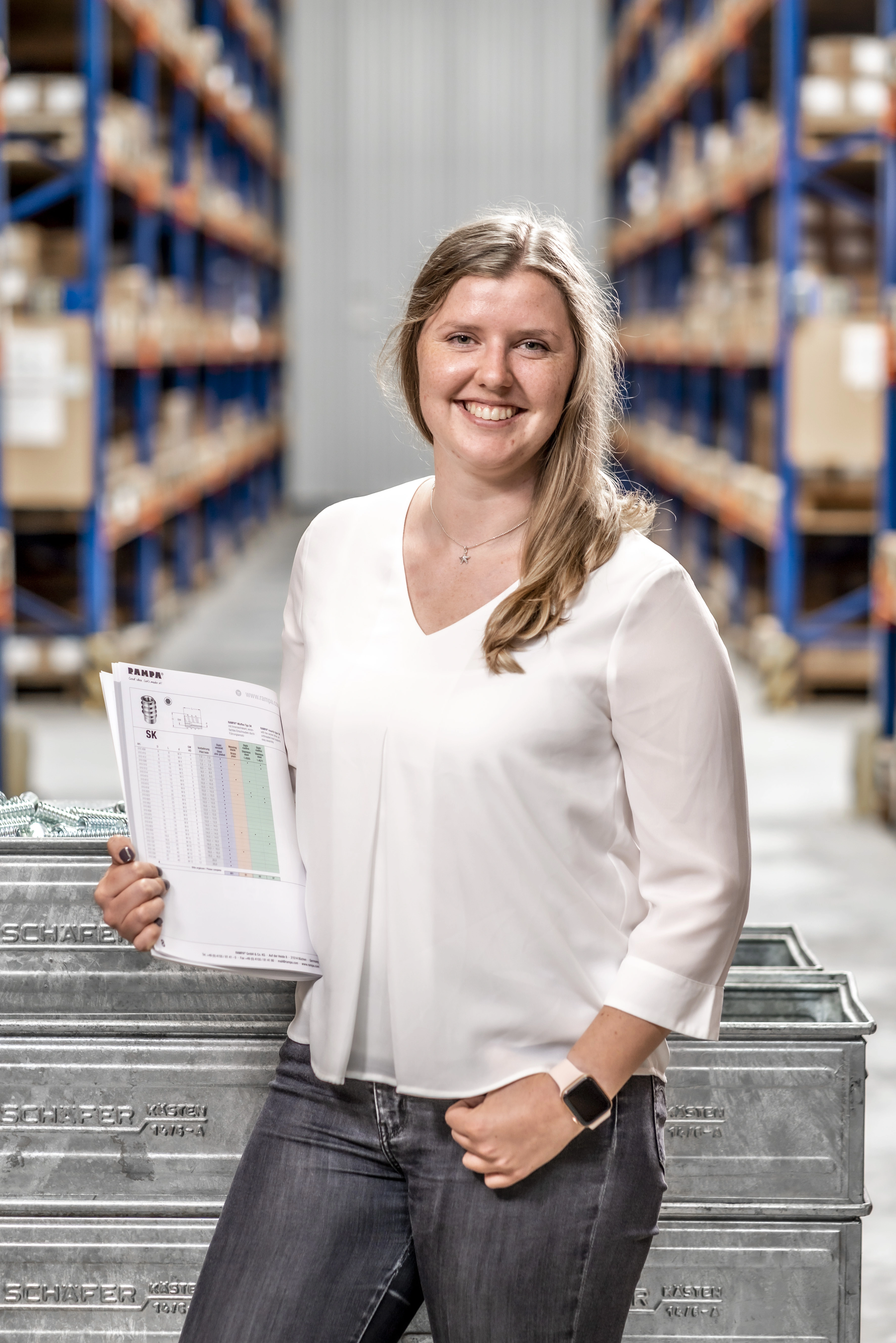 RAMPA Mitarbeiterin Team Versand/Export Eine RAMPA-Mitarbeiterin aus dem Team Versand/Export, die den RAMPA-Katalog in einem Lagerhaus hält.