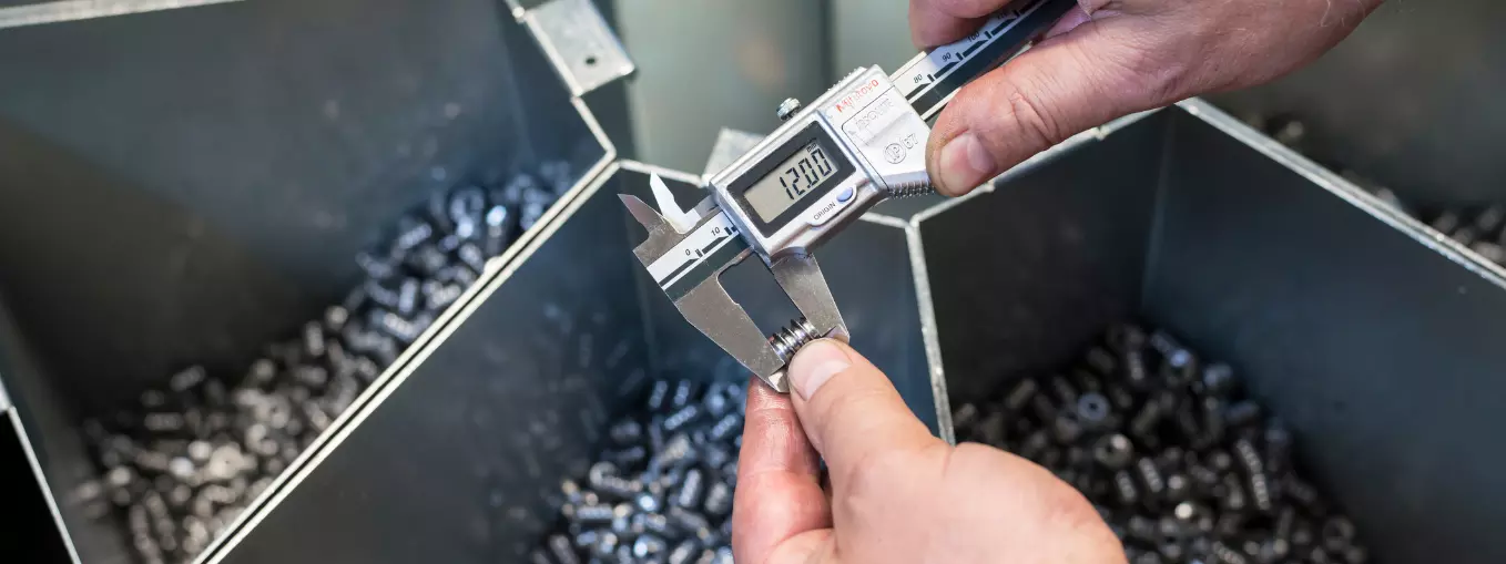 RAMPA: High-quality threaded inserts A RAMPA insert is subjected to quality control with the aid of a caliper. More finished threaded inserts can be seen in the background.