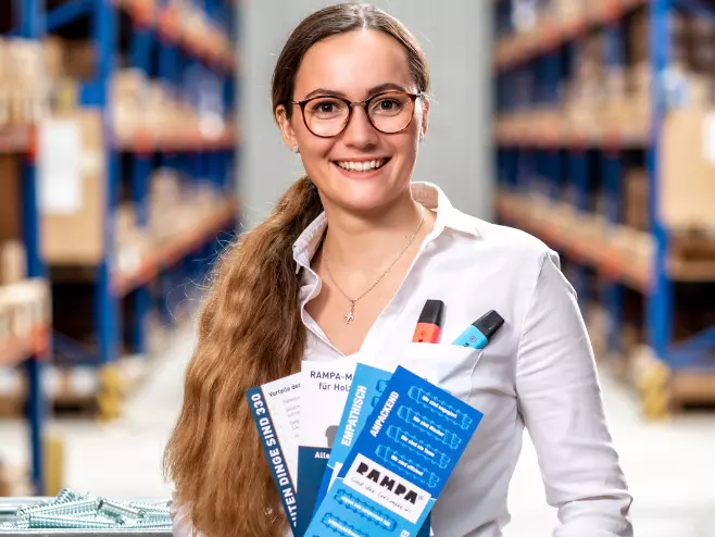 Our teams at RAMPA: Marketing Department A RAMPA employee representing the Marketing team can be seen with flyers in her hand and highlighters in her breast pocket, with the warehouse in the background.