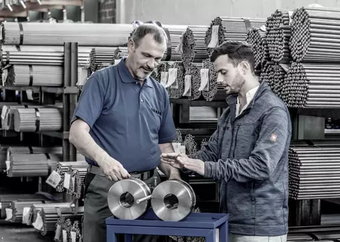 Two RAMPA employees standing in a steel warehouse and exchanging ideas. The picture is meant to symbolize that at RAMPA there is an exchange at eye level across several generations.