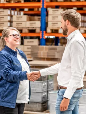 RAMPA's values: We are binding! Two RAMPA employees stand next to each other in the warehouse and join hands. The picture is supposed to stand for RAMPA's value "Commited".