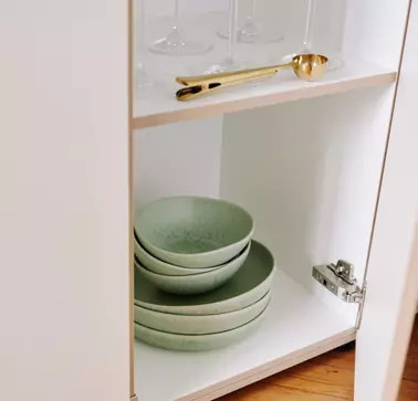 Stocubo is RAMPA's reference partner. A slightly opened cabinet door with decorative contents can be seen. In the cabinet from Stocubo, the hinges that securely connect the carcase and door are processed using RAMPA threaded inserts.