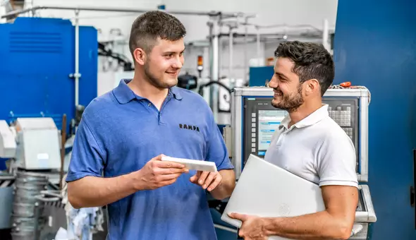 Two RAMPA employees are standing in the production hall having a professional conversation.