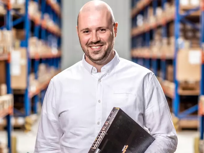 Our teams at RAMPA: IT Department A RAMPA employee representing the IT team can be seen holding IT equipment, with the warehouse in the background.