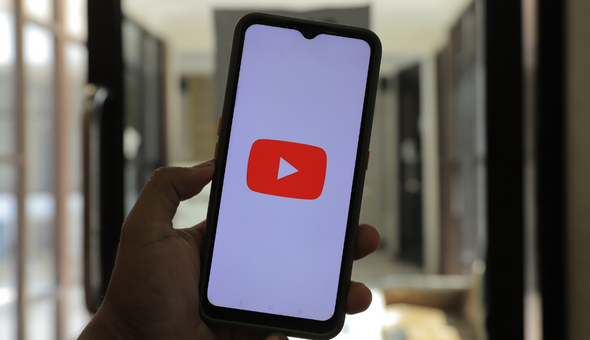 A person holding a cell phone with a YouTube icon. The image is representative of our product videos.