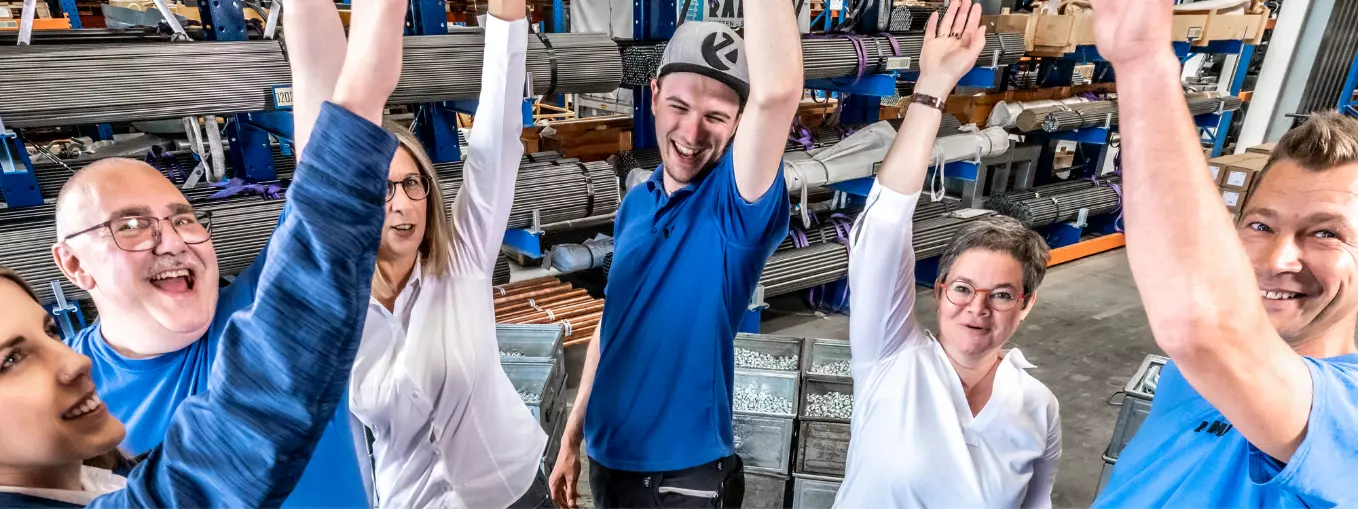Our teams at RAMPA: With team spirit to success A group of RAMPA employees in a warehouse, standing in a circle and throwing their arms in the air together. The picture is meant to symbolize the high team spirit at RAMPA.